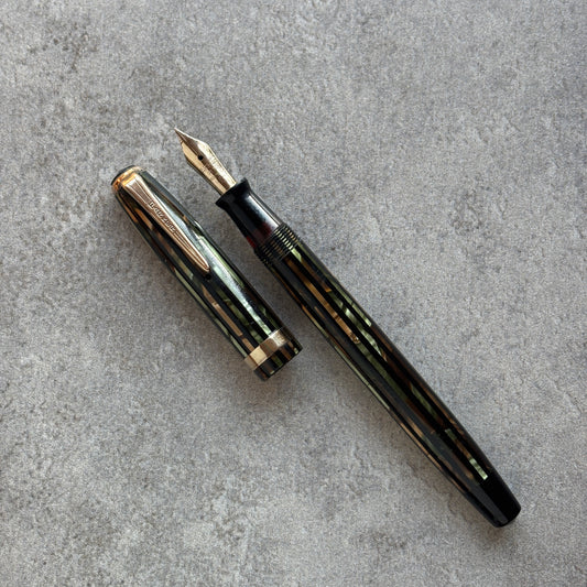 Green and gold Striped fountain pen on a gray concrete surface