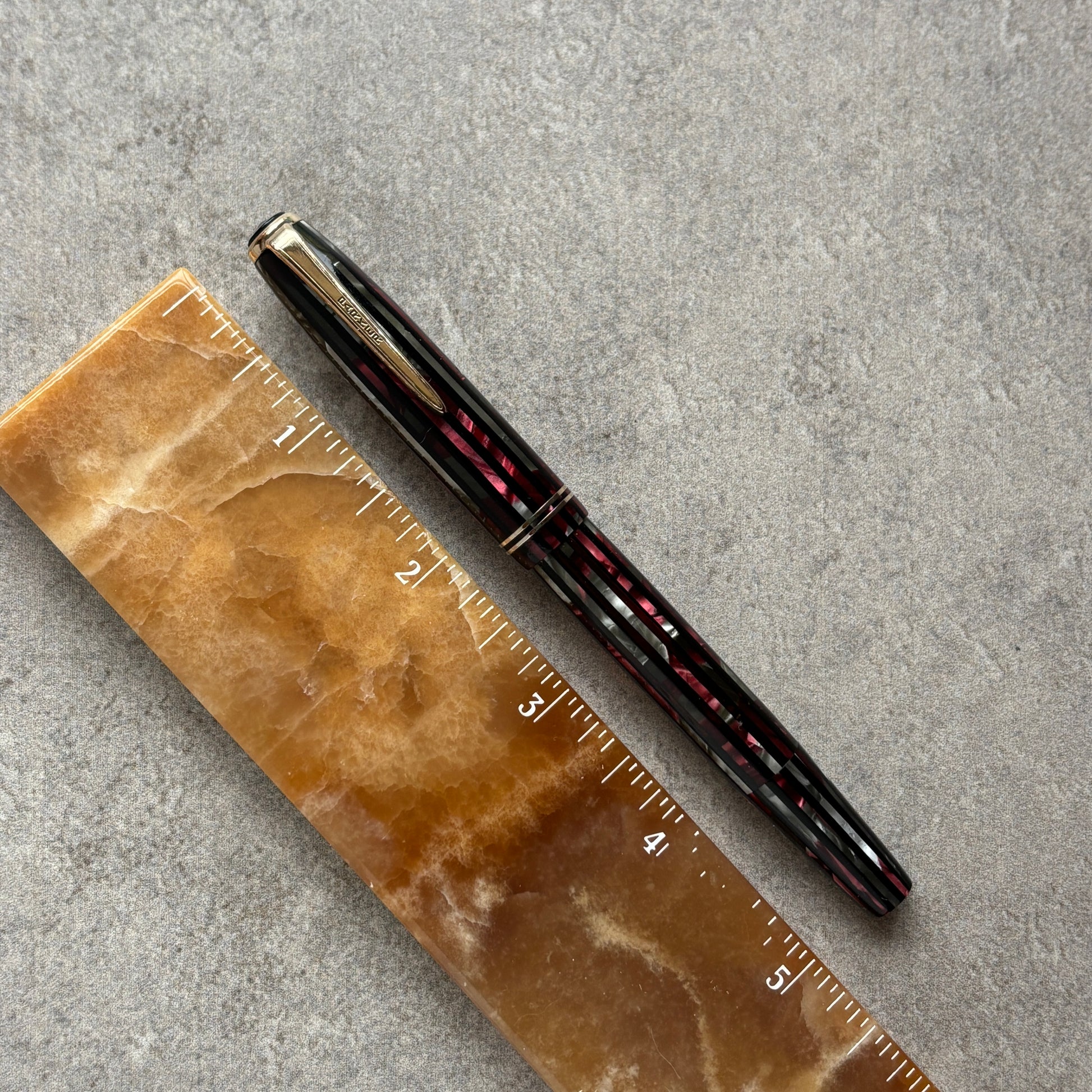 Red and Black pen on a brown marble ruler against a gray concrete background