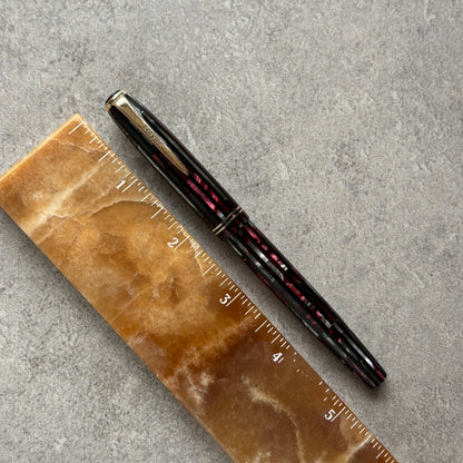 Red and Black pen on a brown marble ruler against a gray concrete background