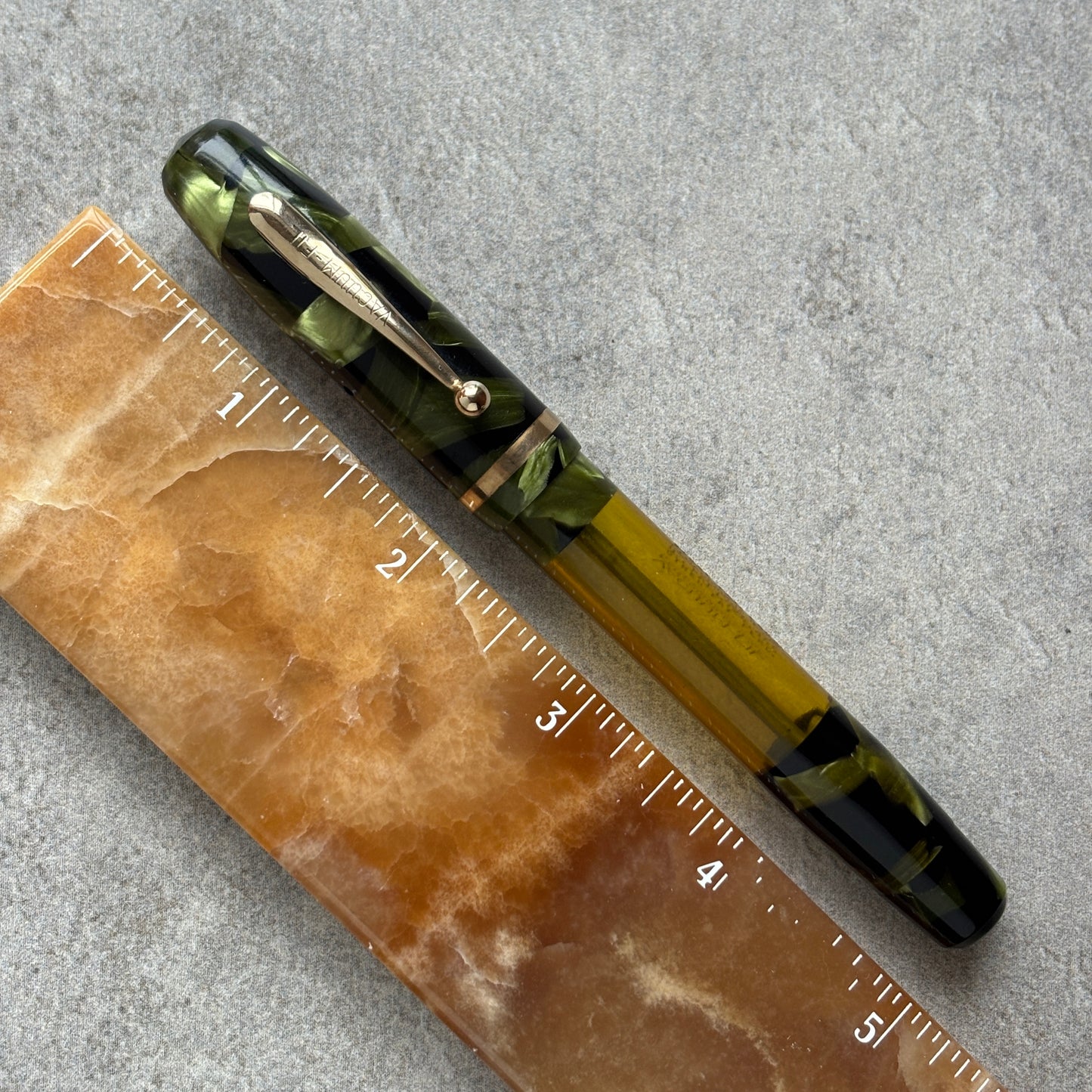 Pen with green and black accents on a textured surface next to a ruler