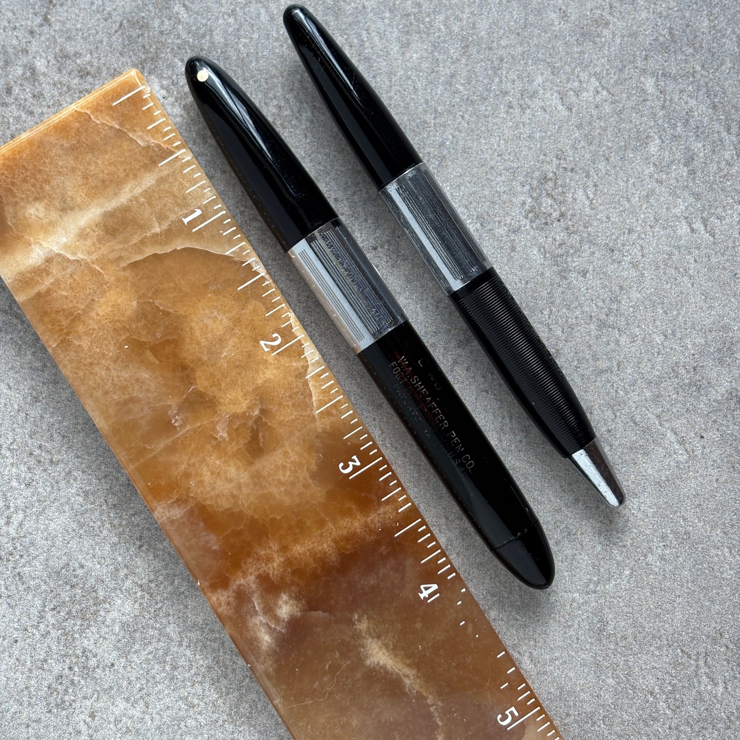 Two black pens on a textured surface with a ruler for scale.