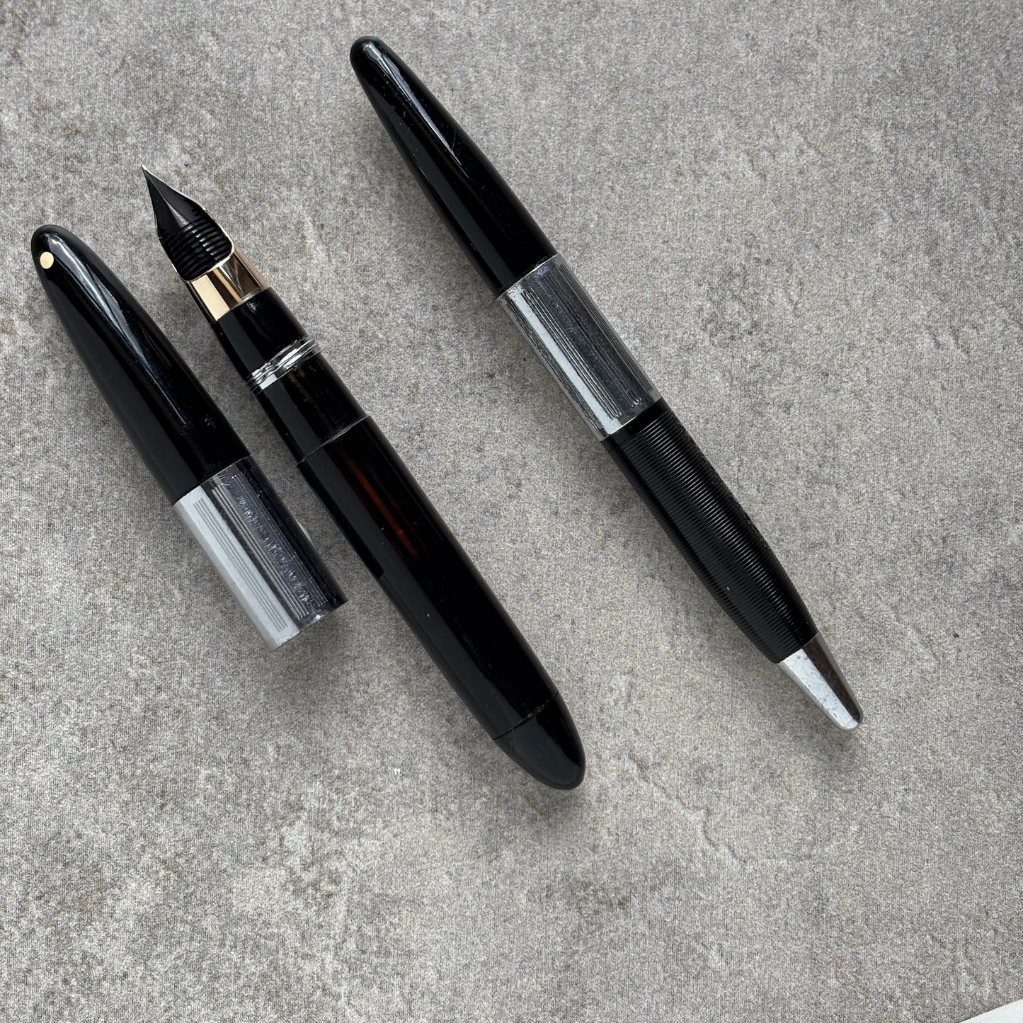 Two black fountain pens on a gray concrete surface