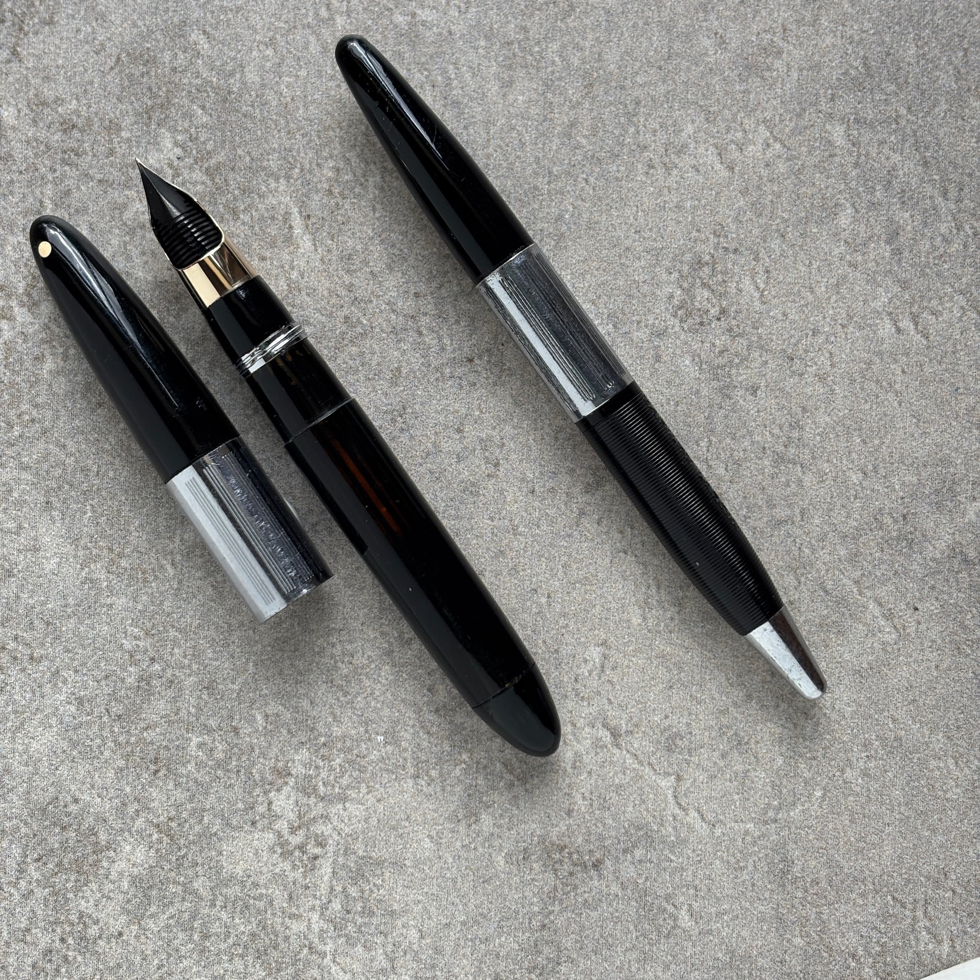 Two black fountain pens on a gray concrete surface