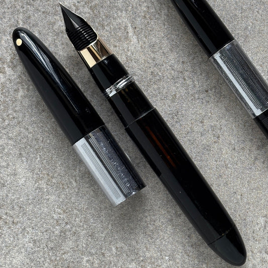 Two black fountain pens on a gray concrete surface