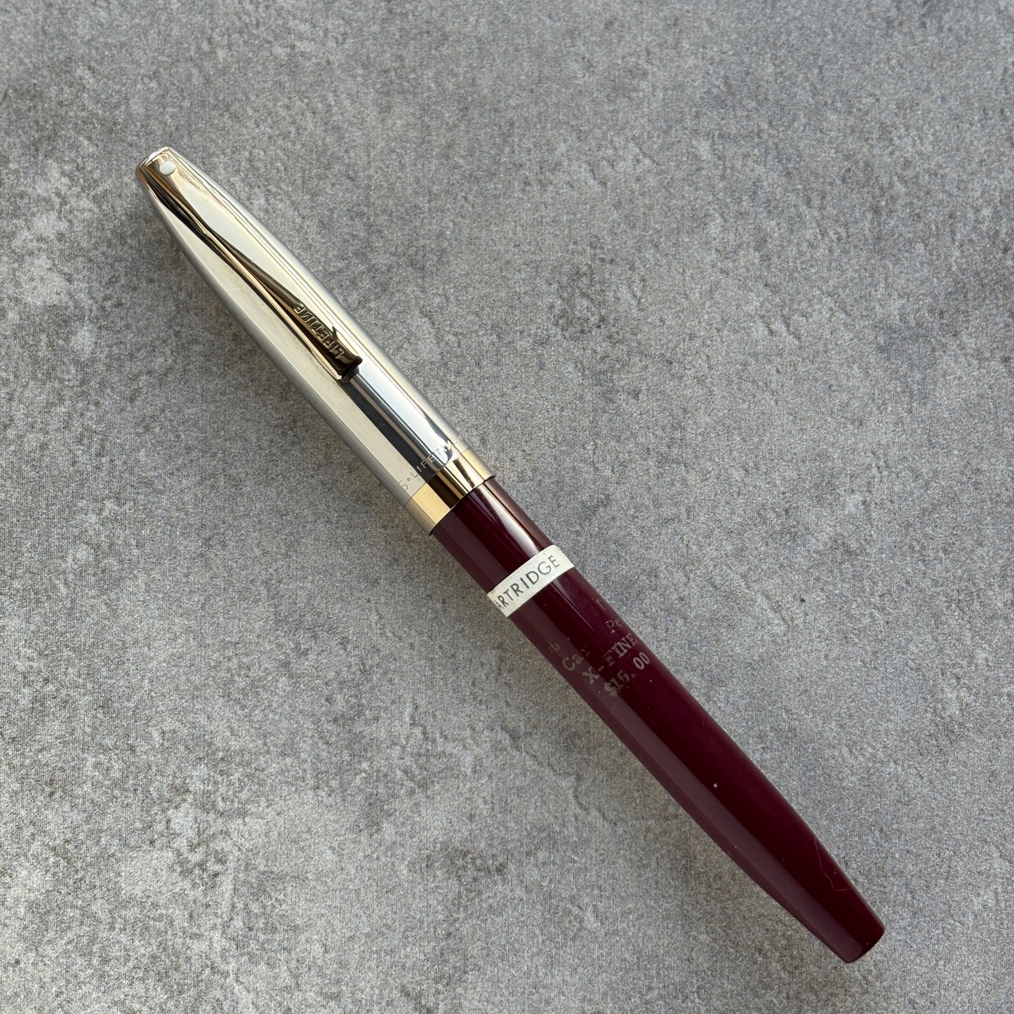 Maroon pen with gold clip on a gray surface