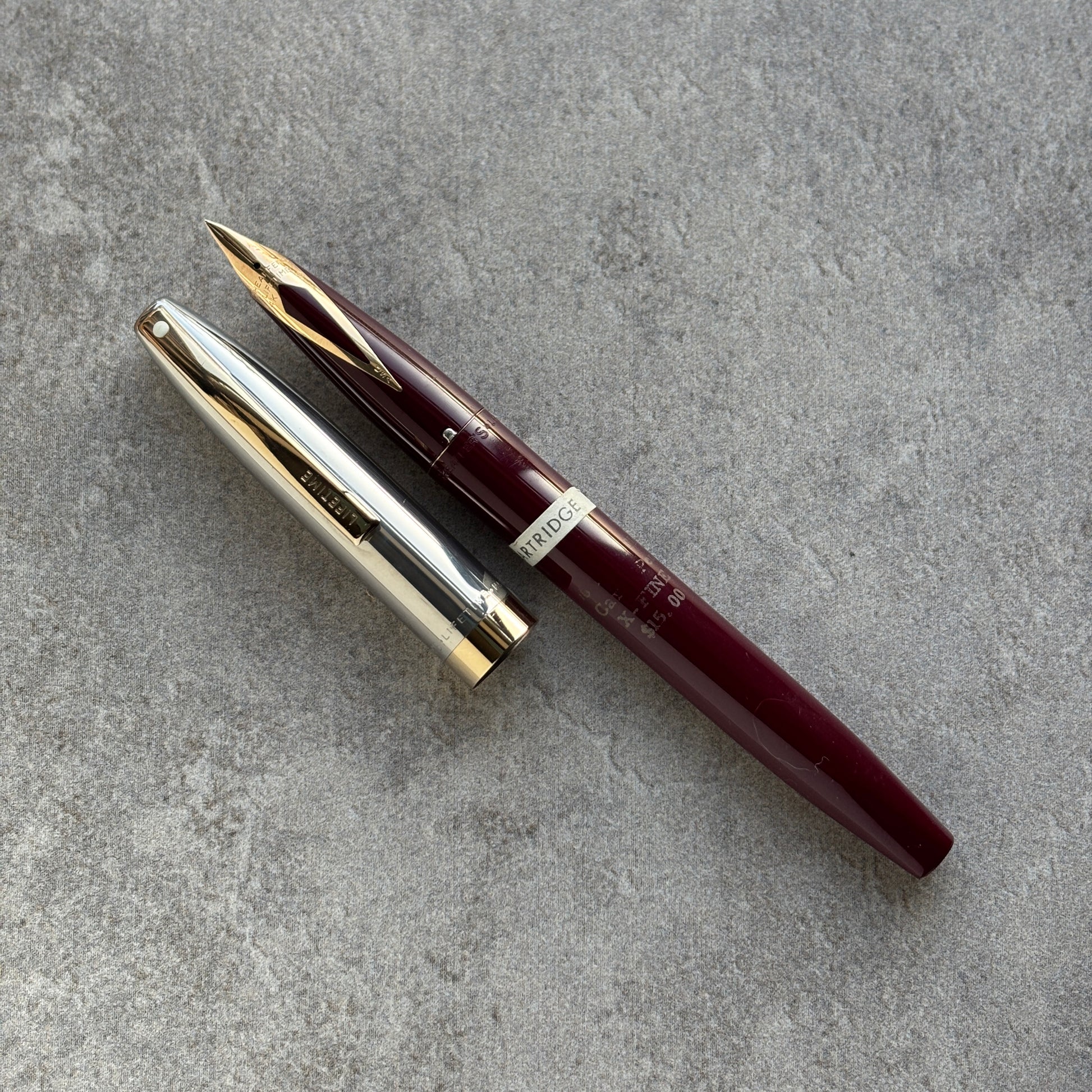 Maroon fountain pen with gold accents on a gray concrete surface