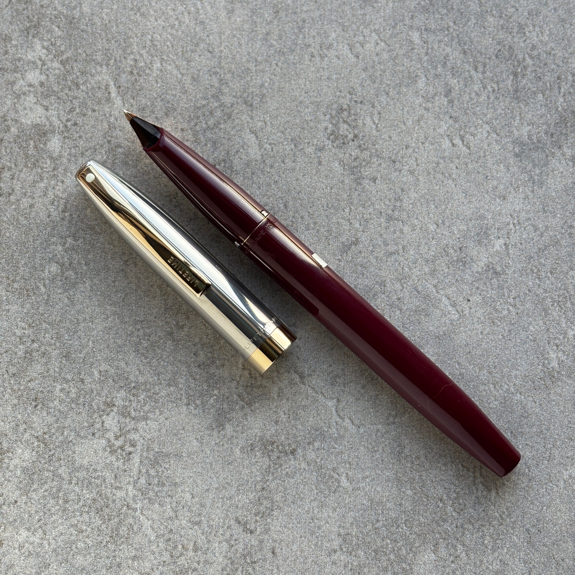 Maroon pen and silver cap on a gray concrete surface