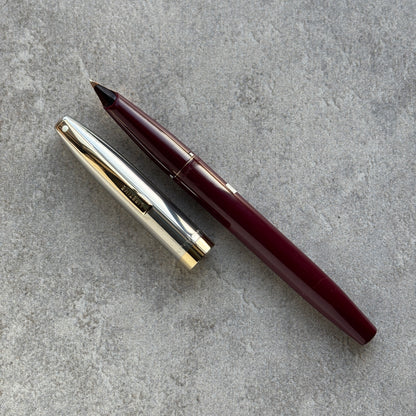 Maroon pen and silver cap on a gray concrete surface