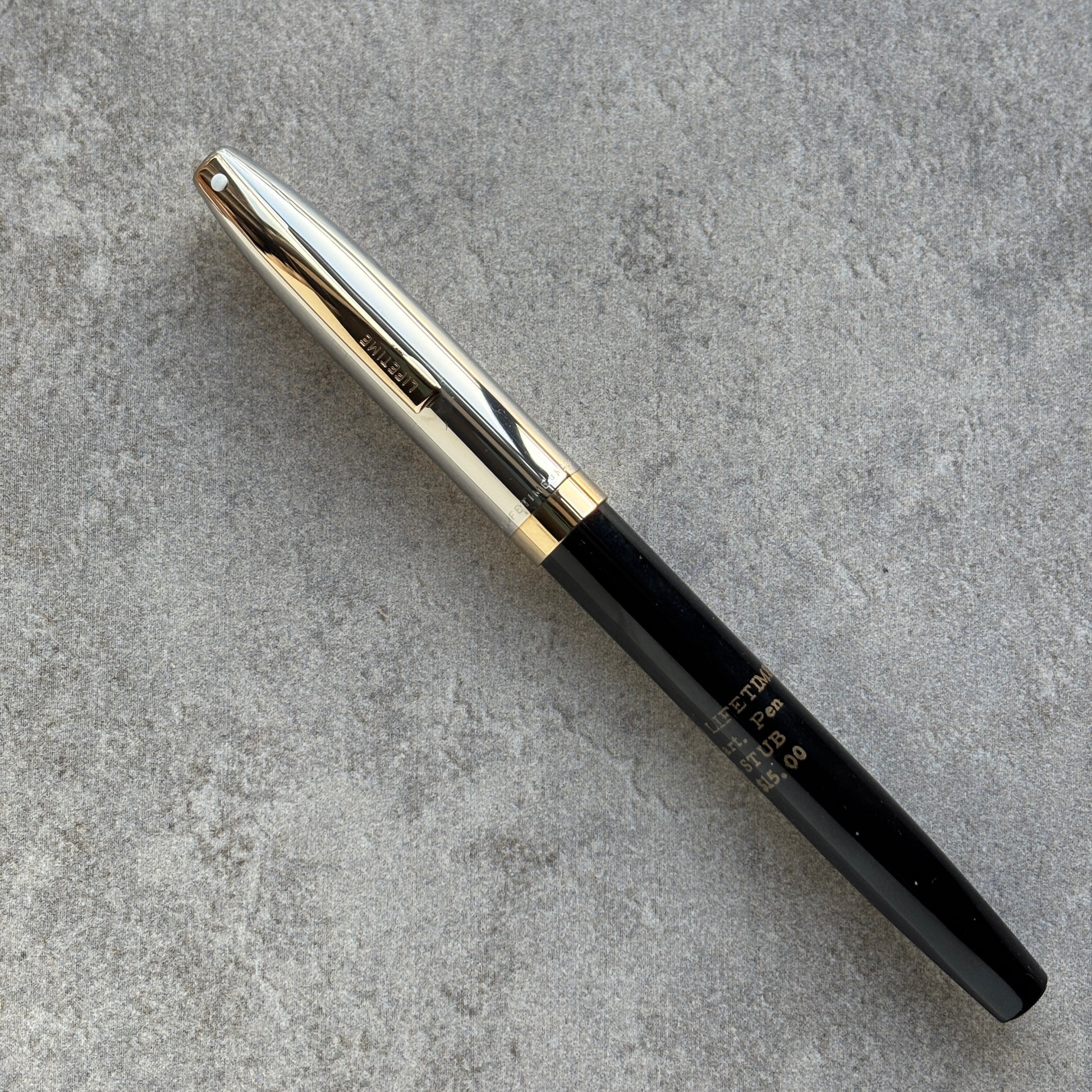 Black pen with gold clip on a gray concrete surface