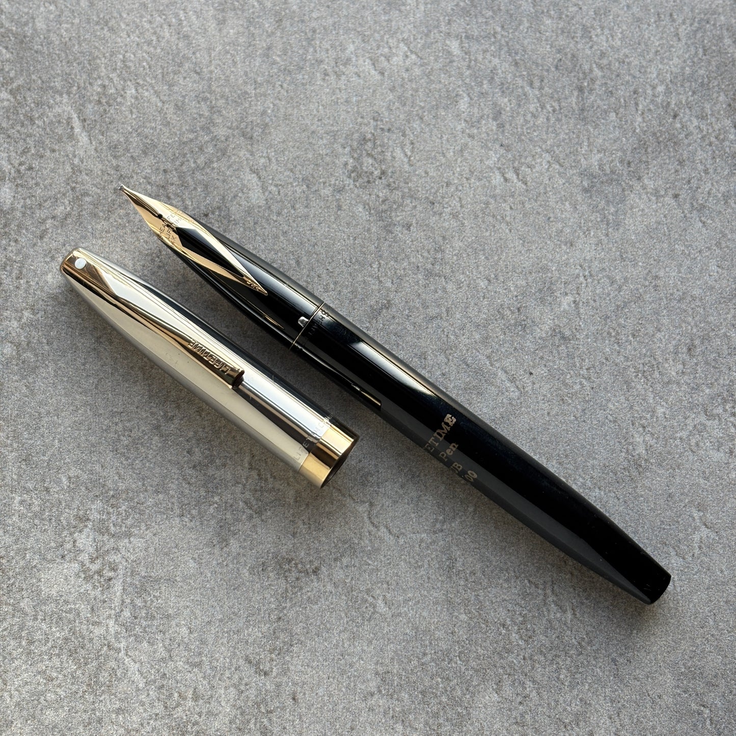 Black and gold fountain pen on a gray concrete surface