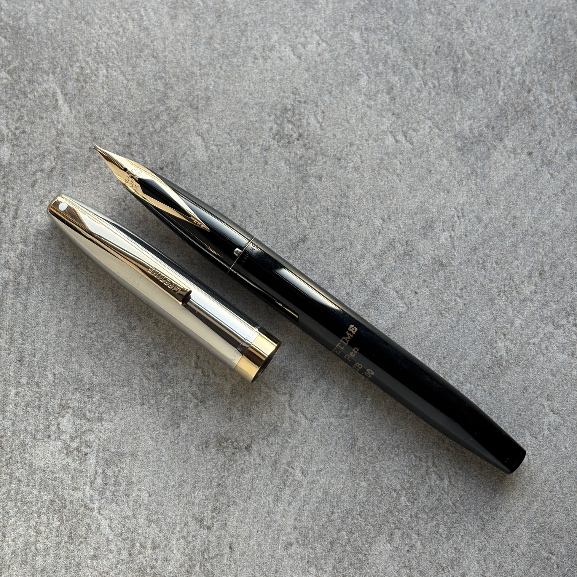 Black and gold fountain pen on a gray concrete surface