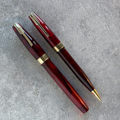 Two red pens with gold accents on a gray surface