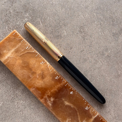 Gold and blue pen on a brown marble ruler against a gray background