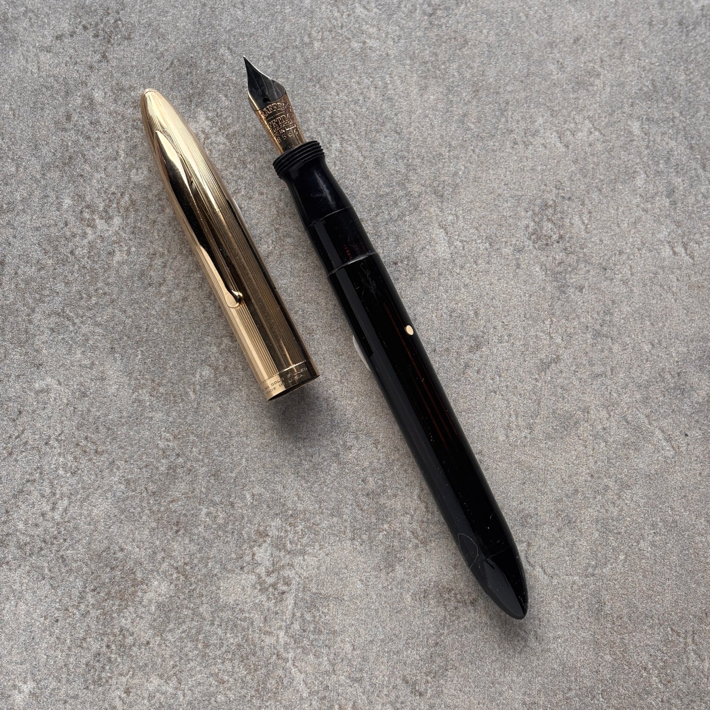 Black fountain pen and gold nib on a gray concrete surface