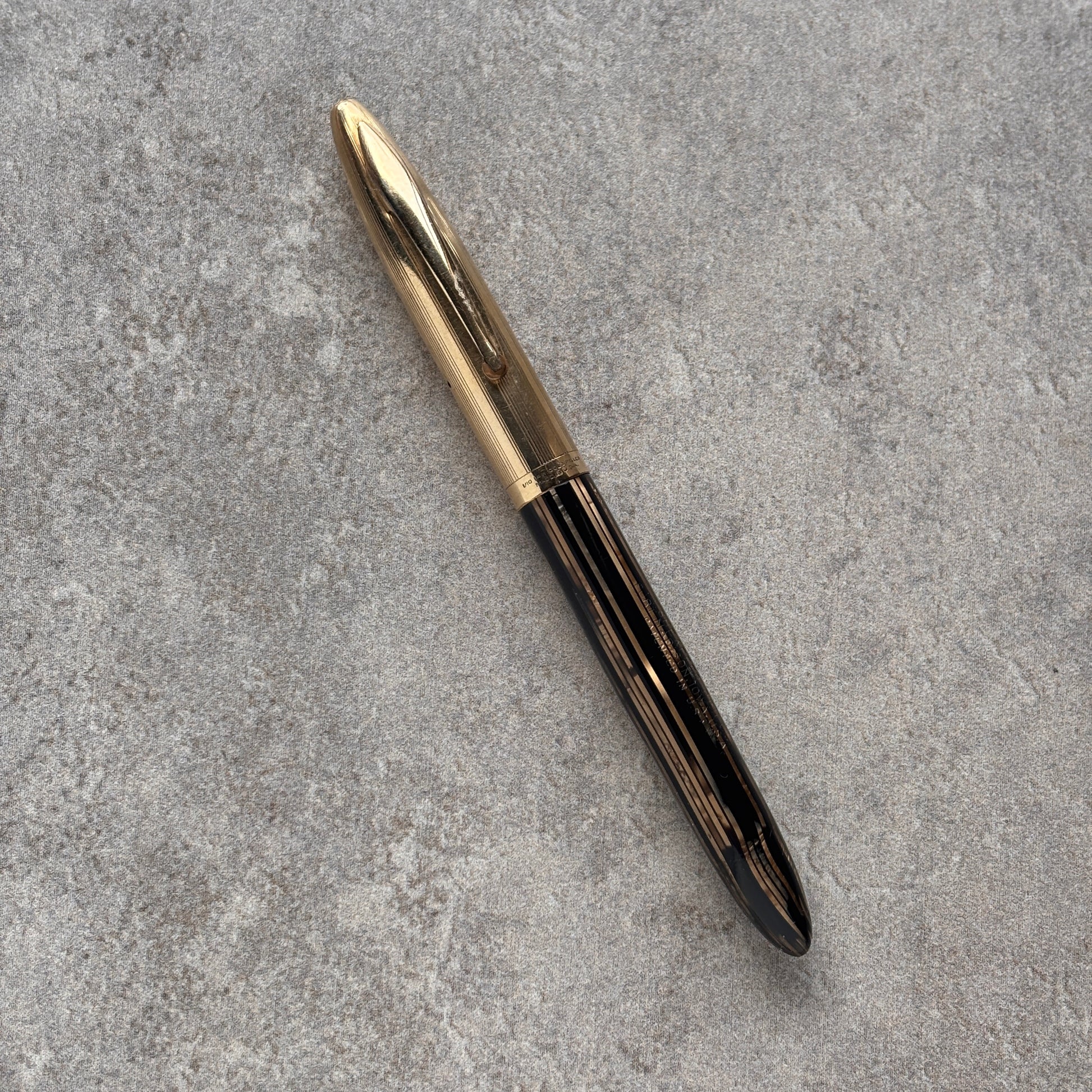 Pen with gold cap and black body on a gray textured surface