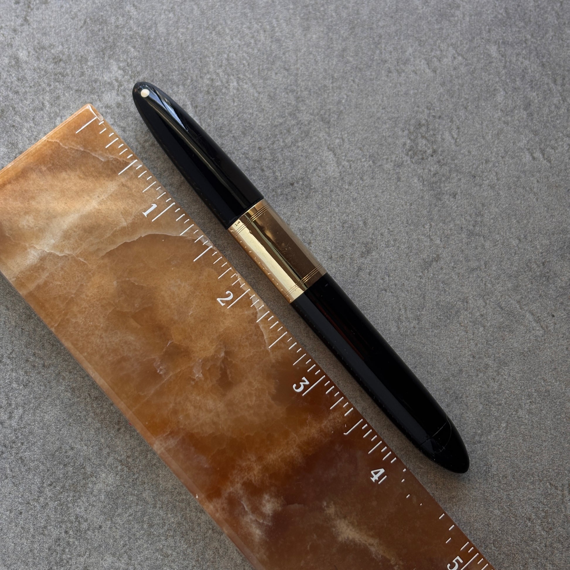 Black pen with gold accents on a brown ruler against a gray background