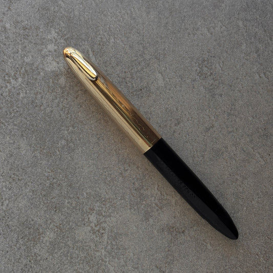 Pen with gold cap and black body on a gray textured surface