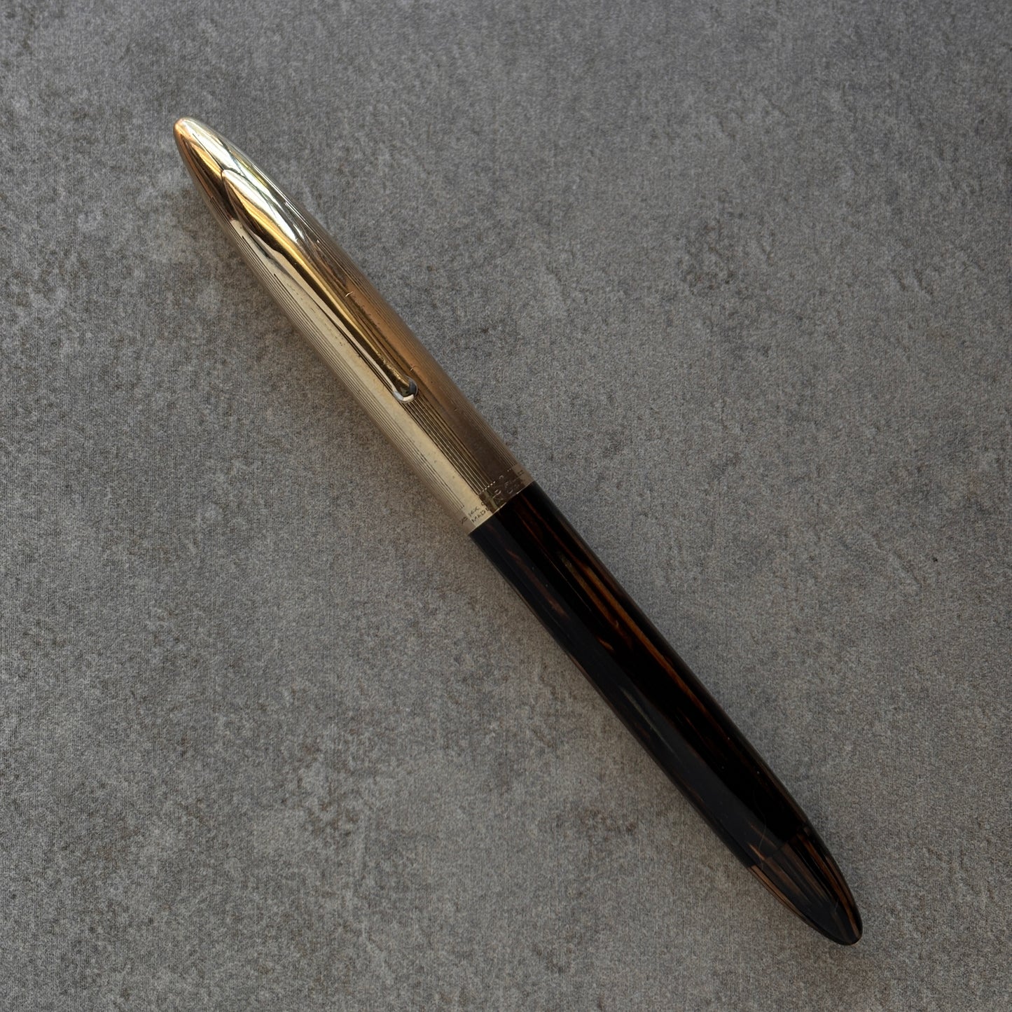 Pen with gold cap and black body on a gray textured surface